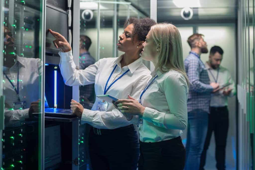 Wide shot of women among server racks in data center room looking at hardware